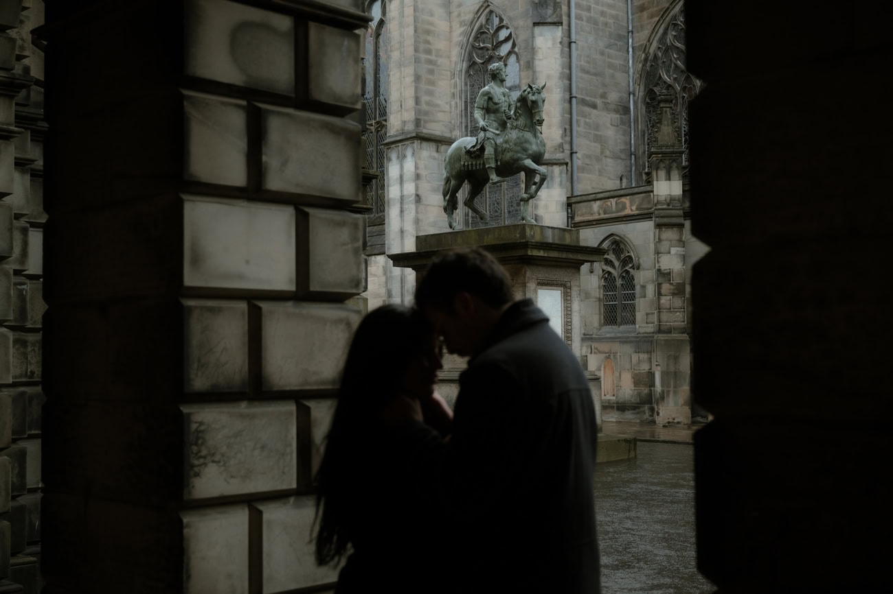 A couple share an intimate moment in silhouette in Parliament Square, Edinburgh, with the bronze equestrian statue of Charles II and the gothic facade of St Giles' Cathedral looming dramatically behind them
