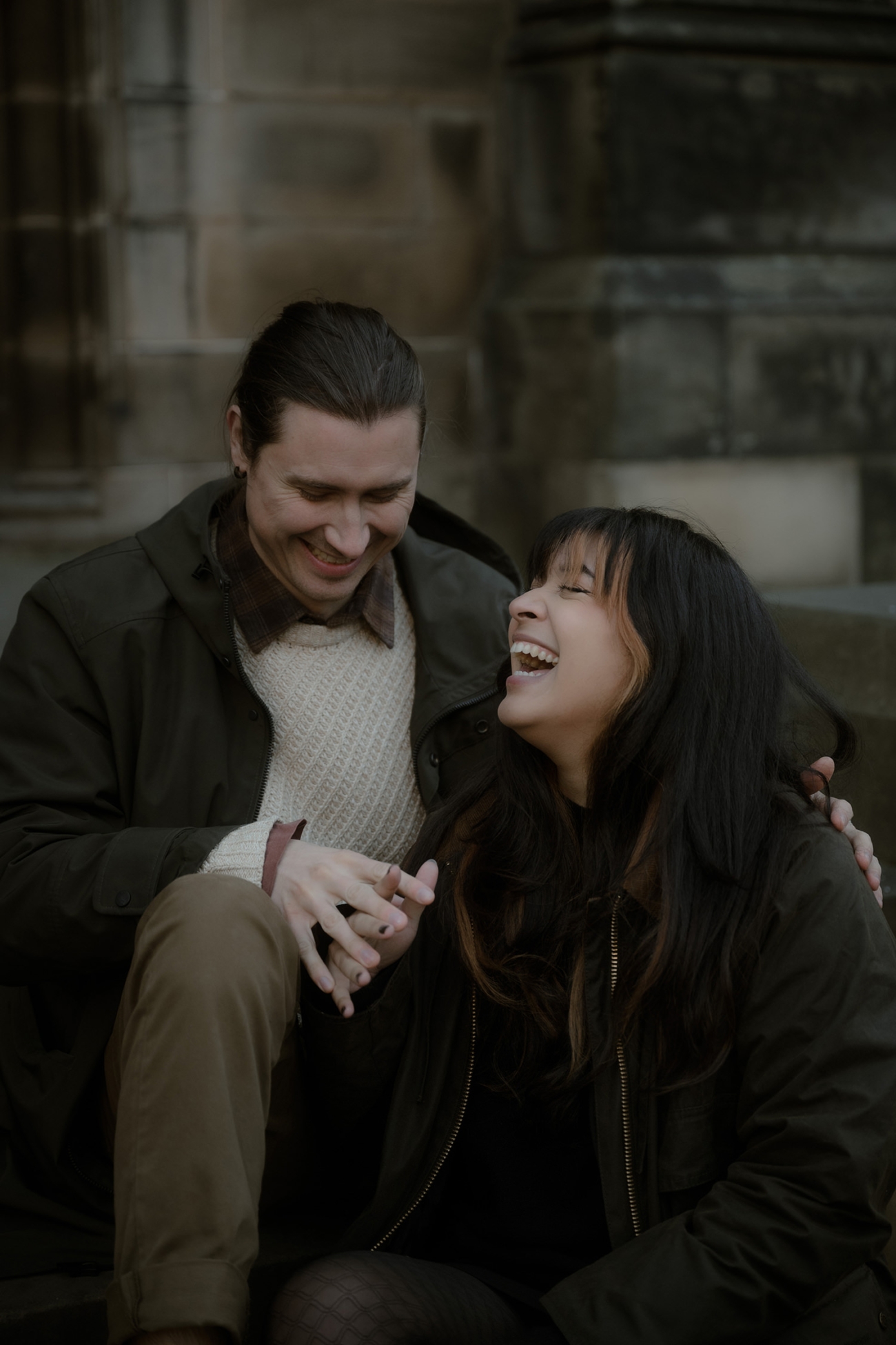 A couple sits together on the steps of St Giles Cathedral, laughing as they hold hands