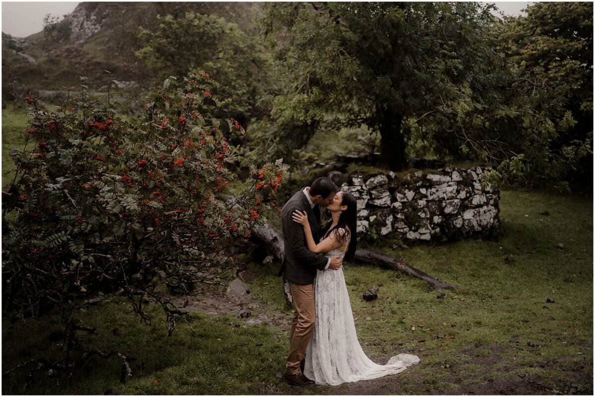 Couple kissing beside a rowan tree heavy with red berries at Fairy Glen, Isle of Skye, with an old stone wall behind them