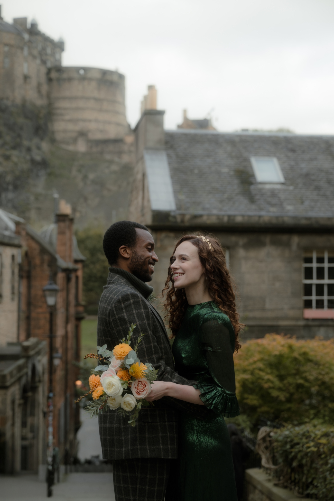 Groom lifting bride in front of Edinburgh Castle, surrounded by autumn foliage and historic stone buildings