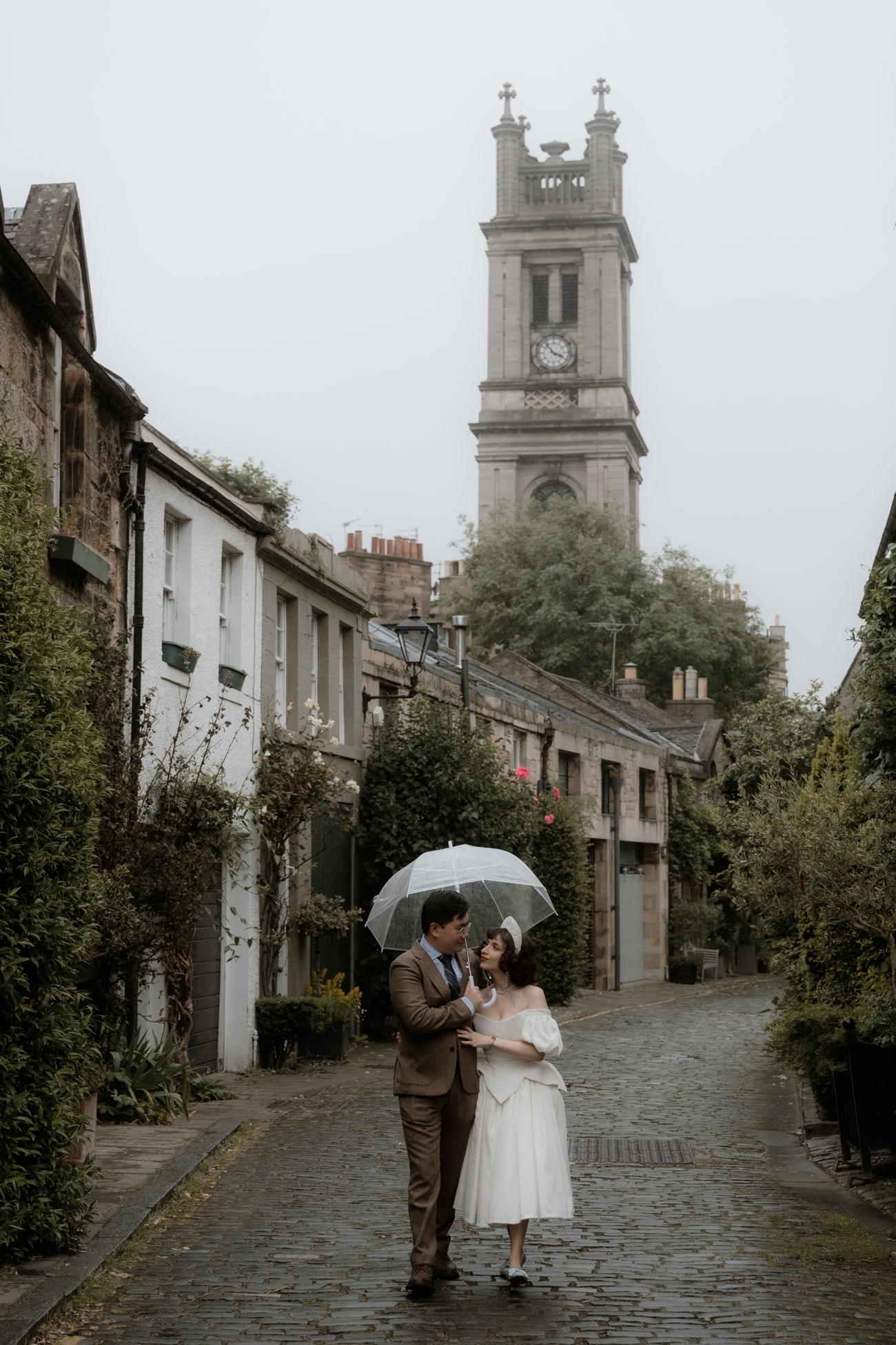 Bride and groom walking down Circus Lane on their rainy wedding day, looking at each other whilst the groom puts an arm around the bride