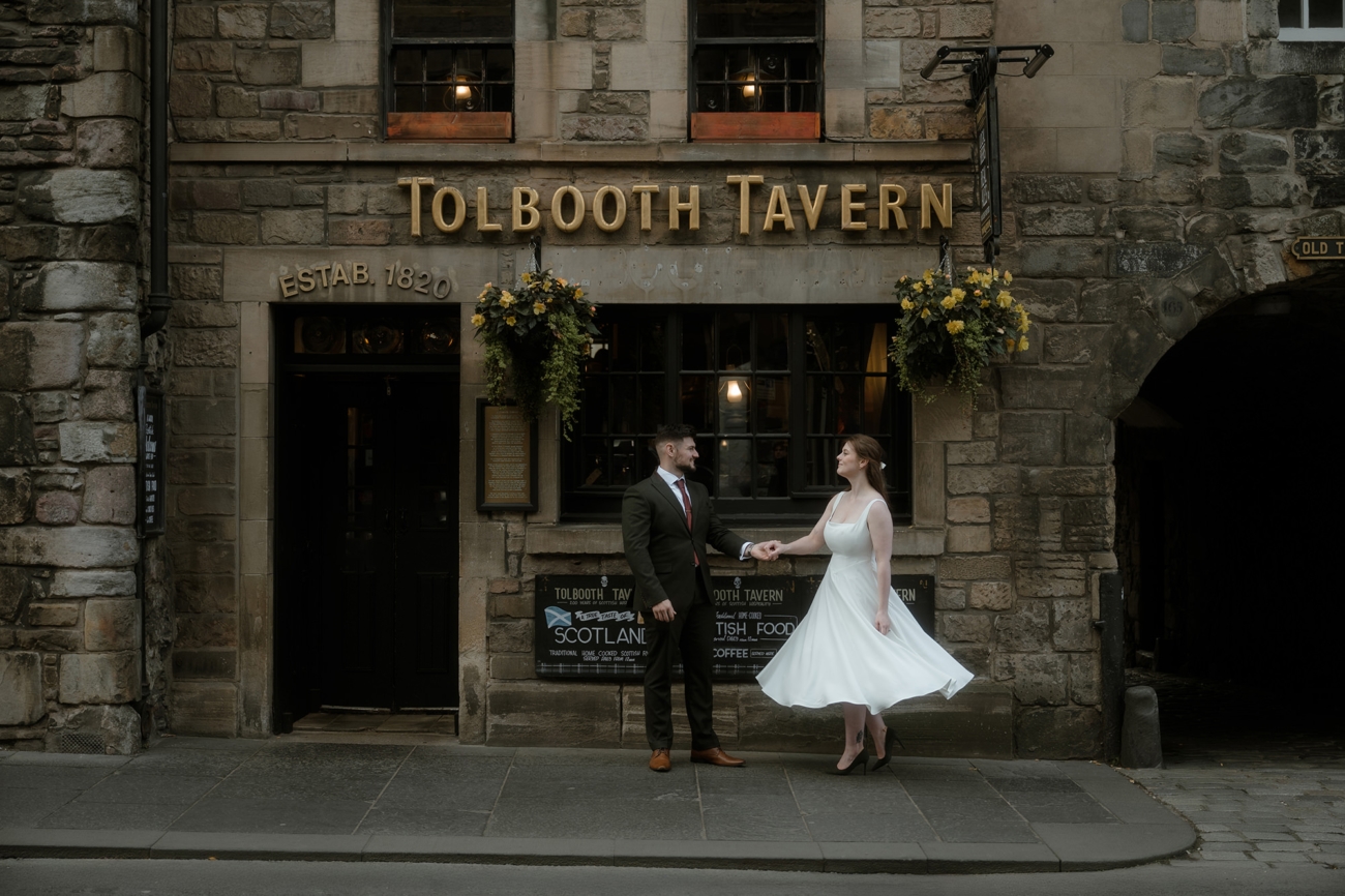 Bride and groom outside the historic Tolbooth Tavern on Edinburgh’s Royal Mile, with the stone facade, hanging flower baskets, and gold signage visible