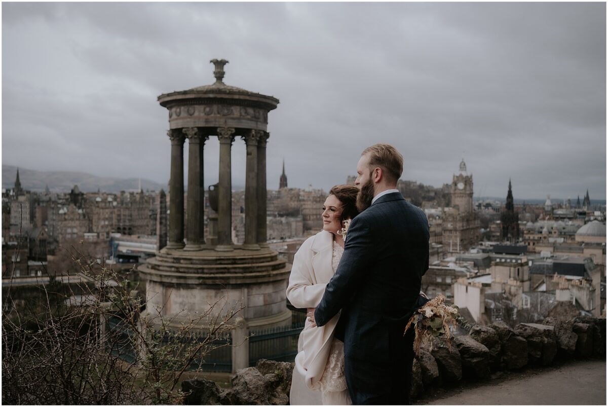 Calton Hill elopement photos in Edinburgh - windy couple portaits with the city skyline in the background, bride's hair windswept on a cold day