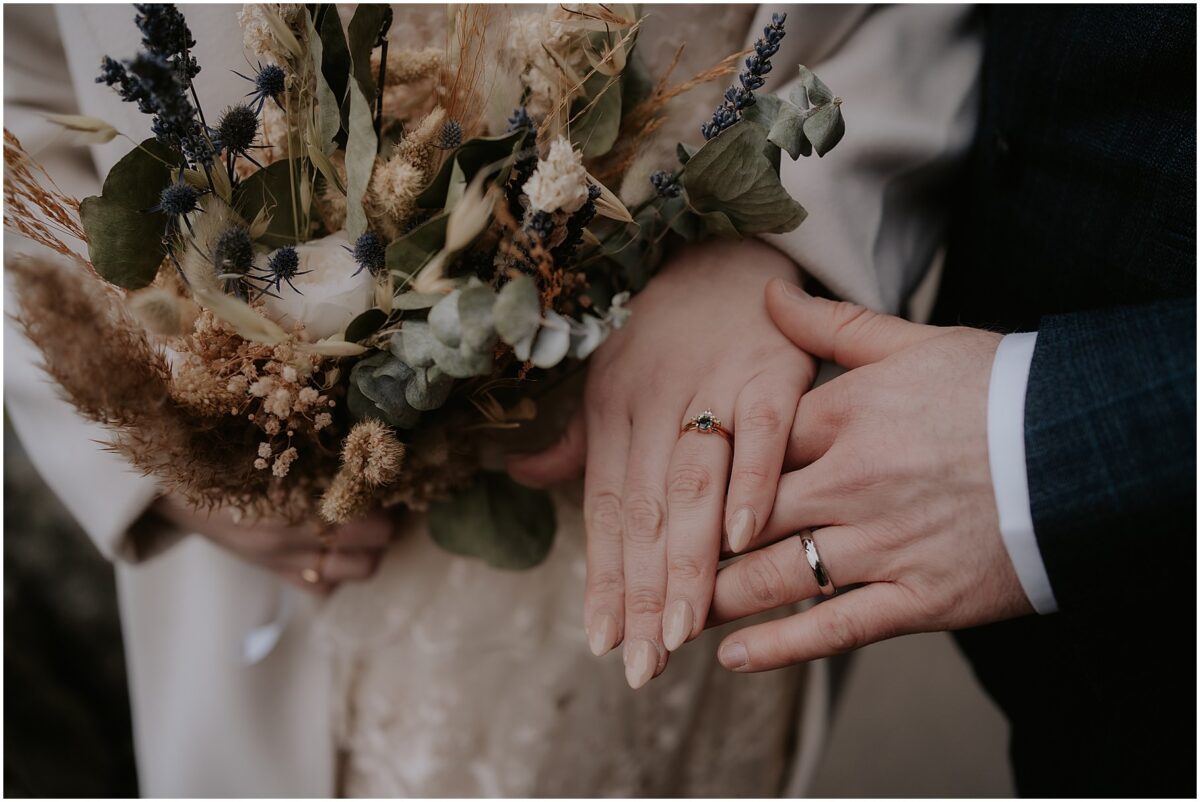 Bridal bouquet held next to the hands of newlyweds with a close-up image of their wedding rings