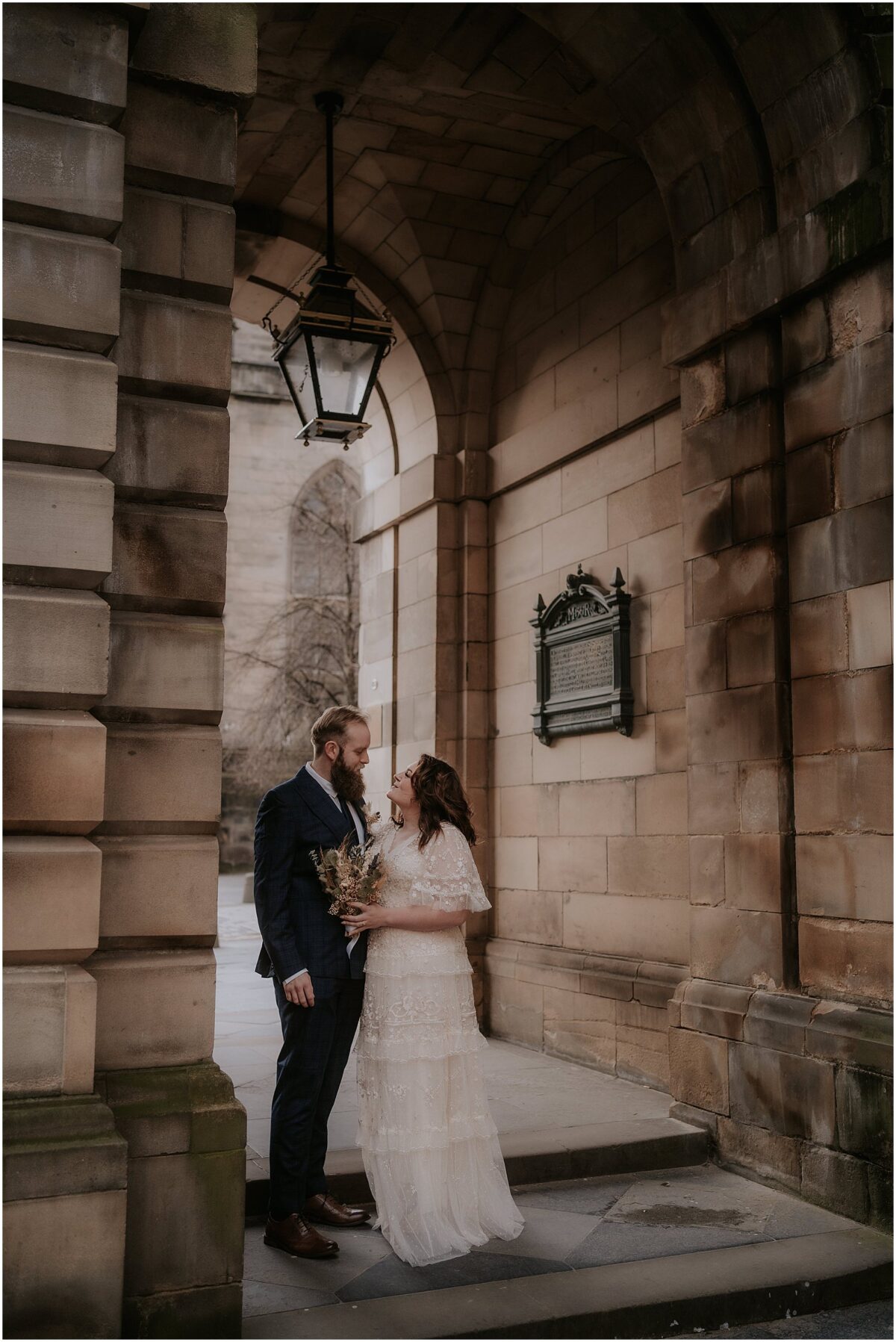 Newlyweds standing closely in the arches of Royal Mile