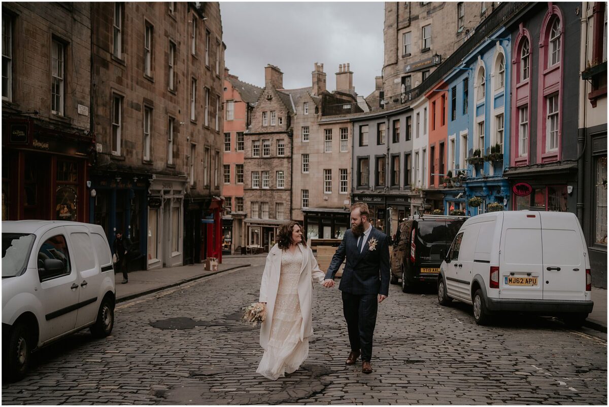 Bride and groom walking on Victoria Street, colourful buildings and parked cars surrounding them