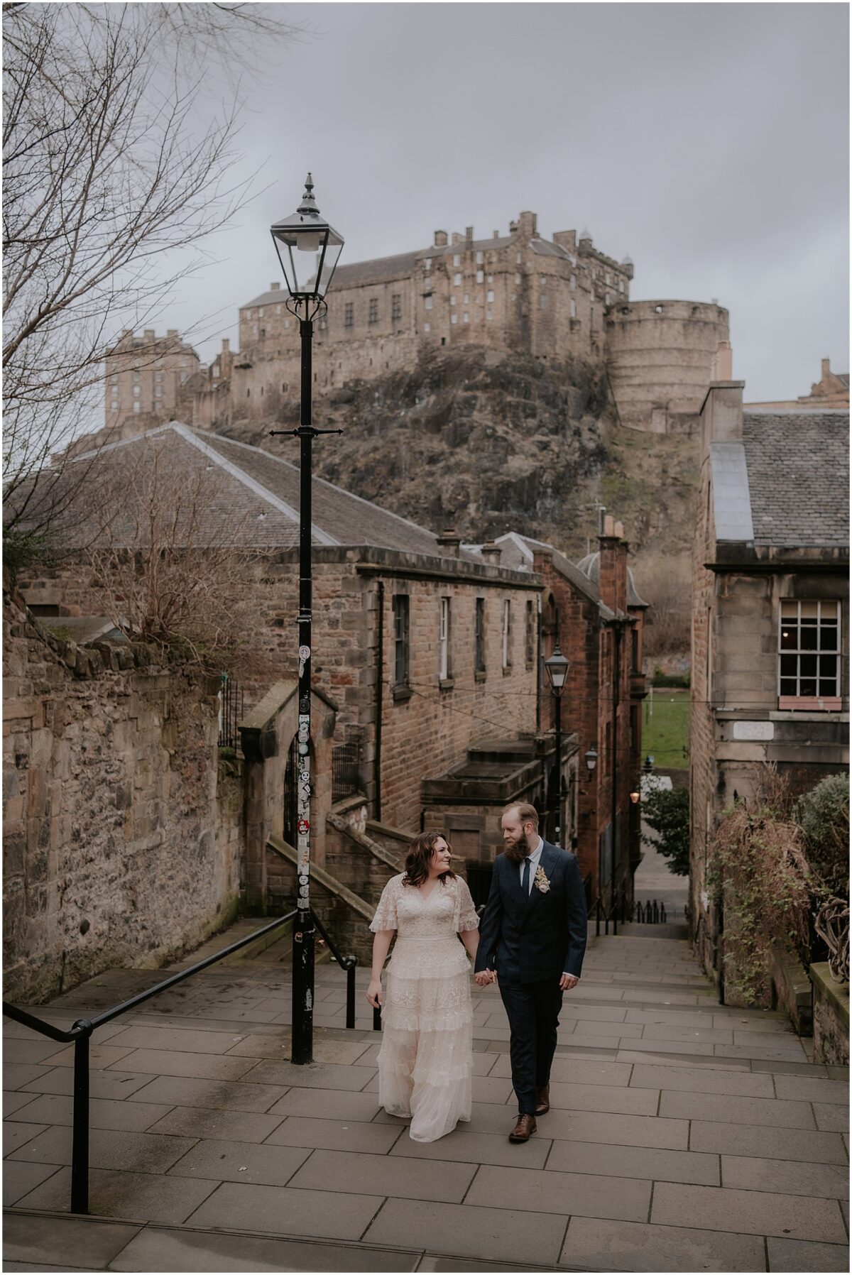 Bride and groom standing at the top of Vennel Steps with Edinburgh Castle towering in the background