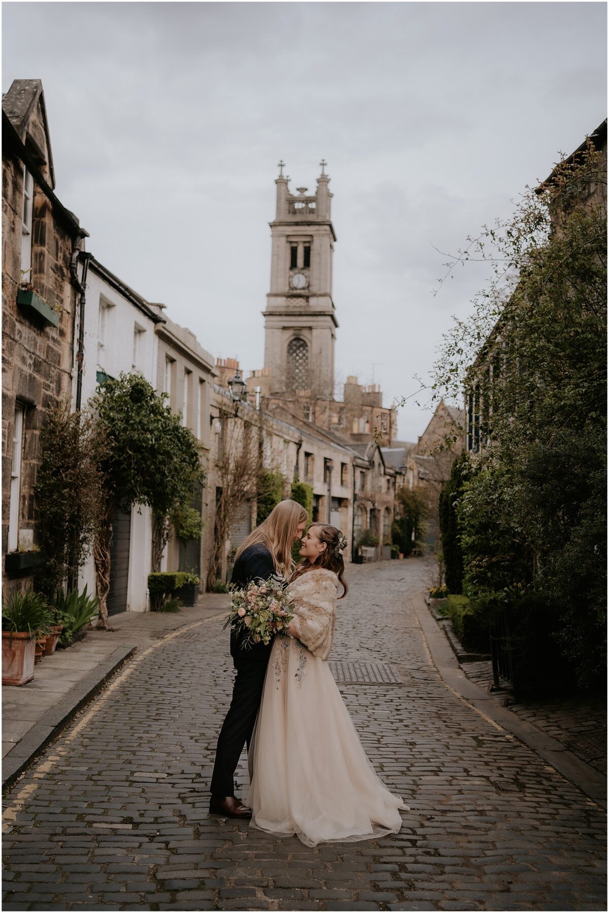 Married couple is a close embrace with a tall clock tower behind them
