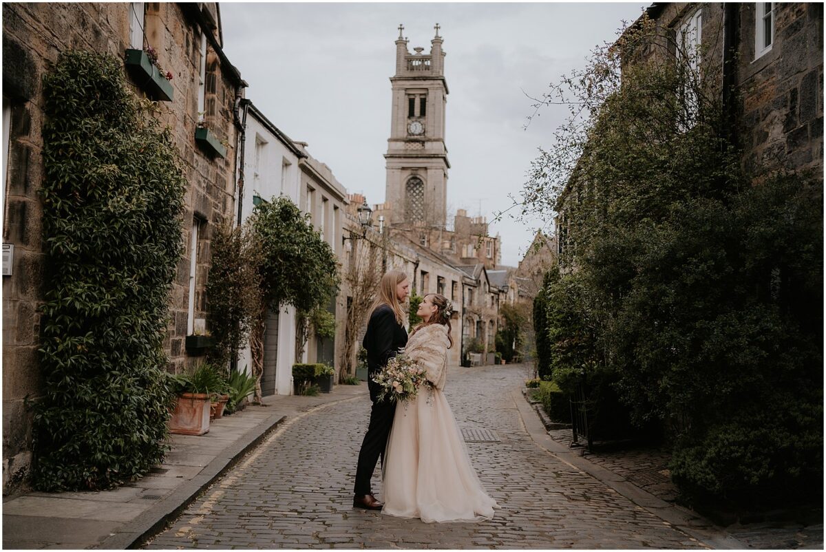 Bride and groom facing each other whilst standing in the middle of cobblestone street