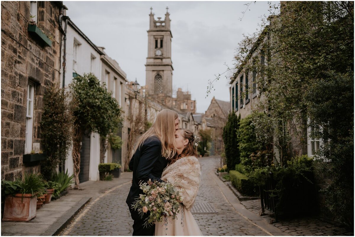 Groom planting a kiss on bride's forehead with the street's green vegetation surrounding them
