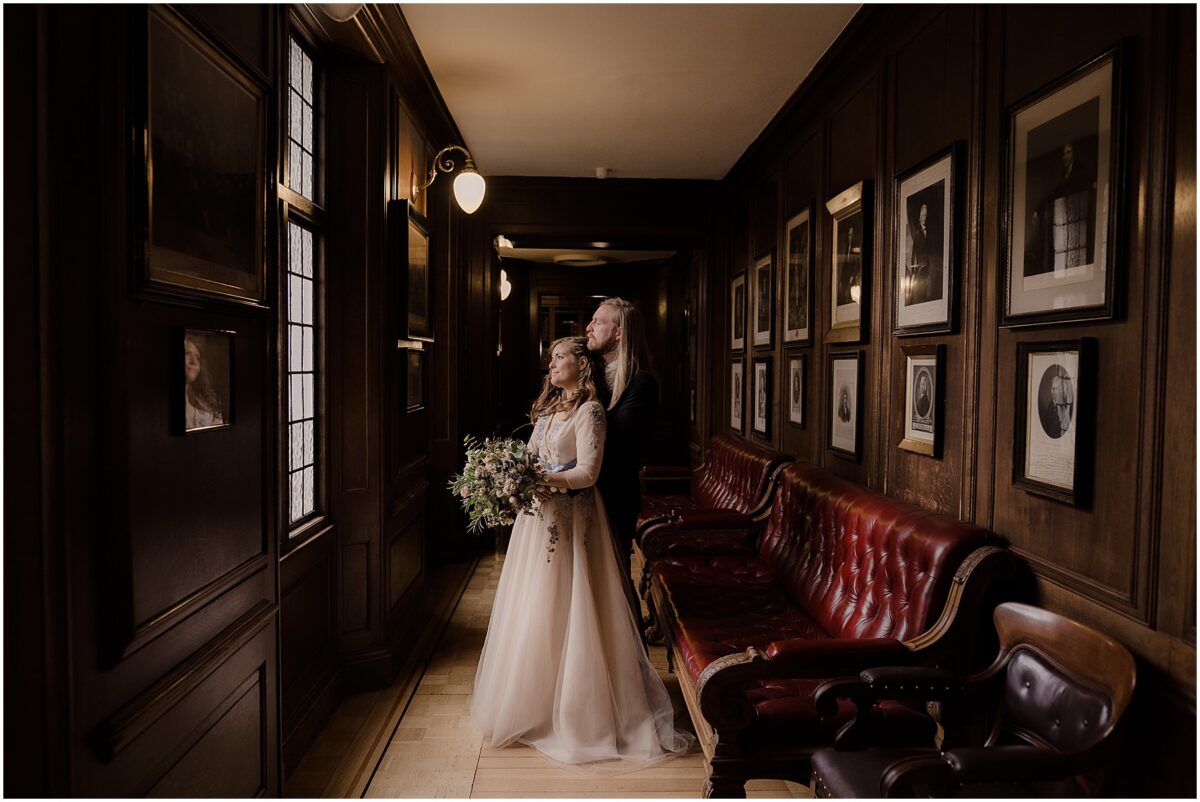 Close embrace of the newlyweds in the corridor of the venue, both looking out the window