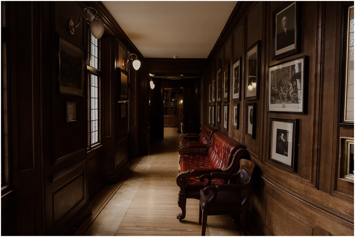 Wooden hallway with old burgundy furniture and old photographs of doctors hanging on the walls, leading to the ceremony room