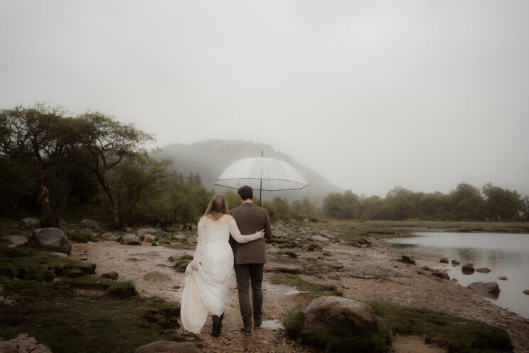 Bride and groom walking in the rain under an umbrella at their wedding