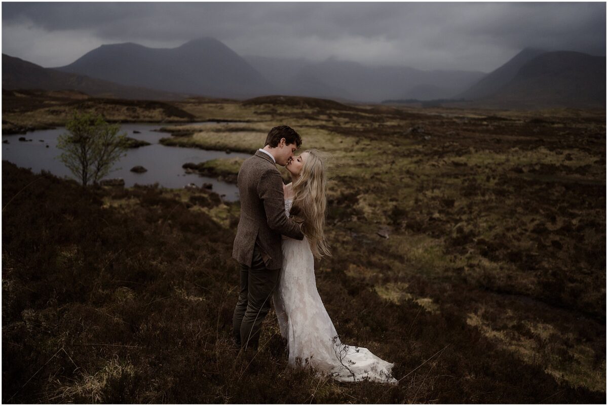 Bride’s white train fans out behind her as she leans into the groom’s chest - mountain Rannoch Moor elopement