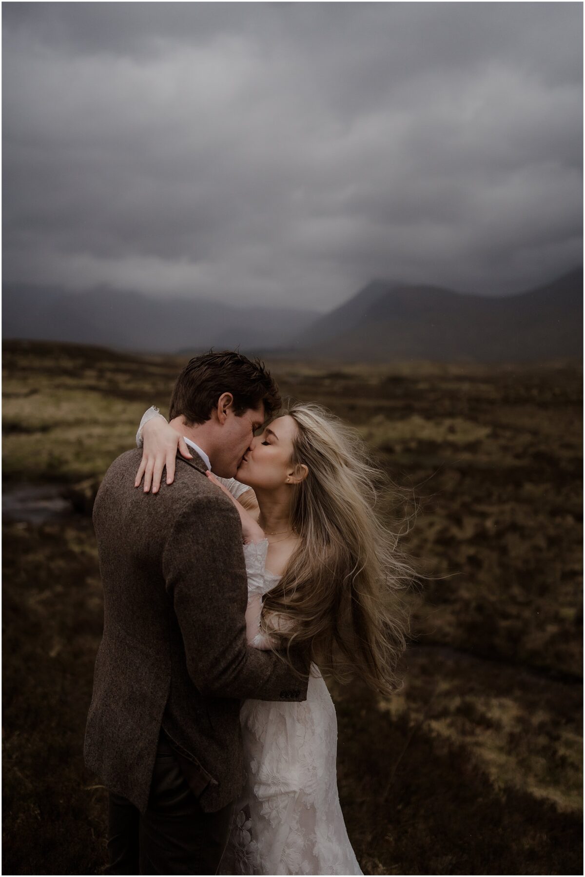 The bride and groom share a gentle kiss atop a heather-covered ridge of Rannoch Moor