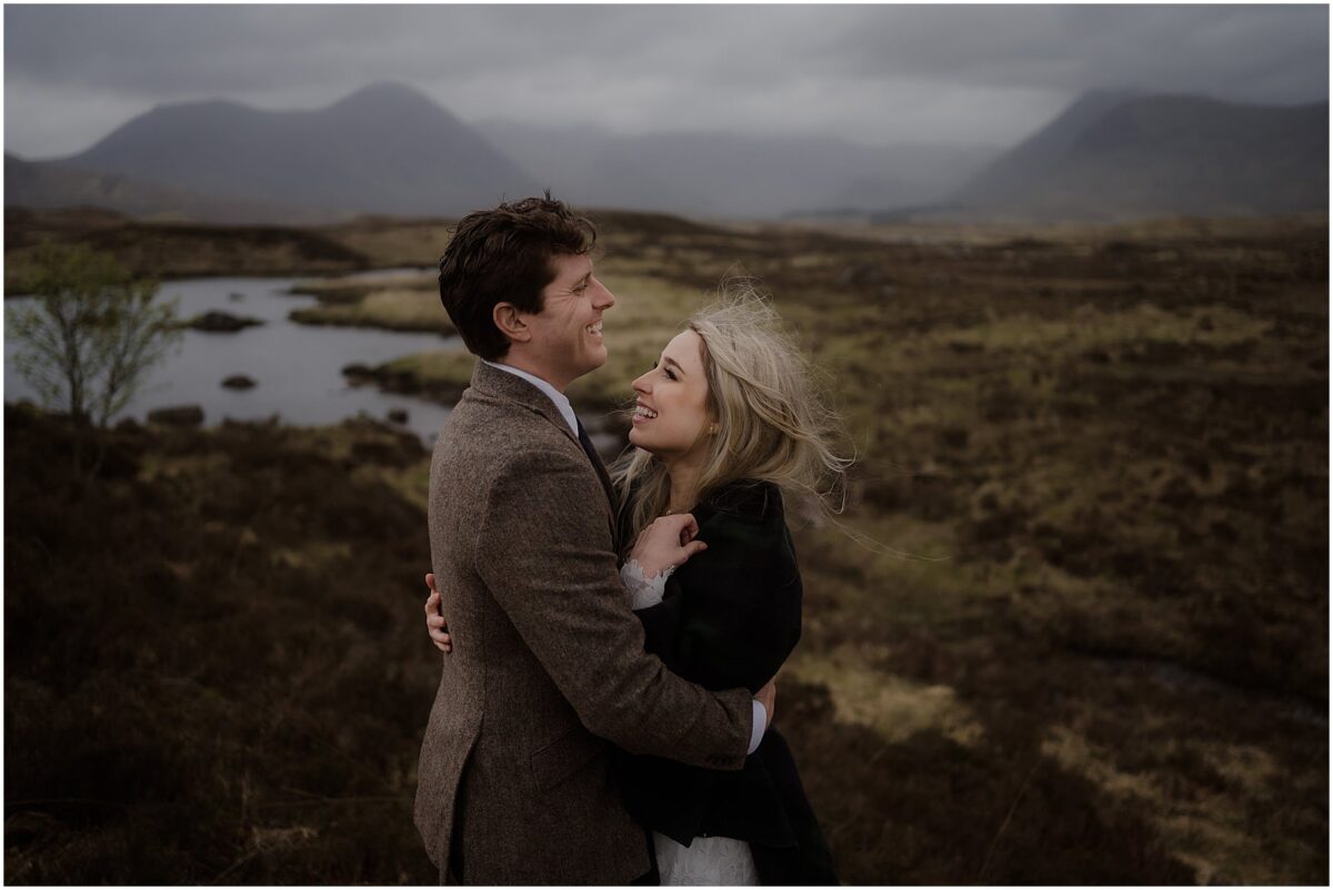 Groom hold the bride tightly whilst they both laugh surrounded by moody Scottish highlands landscapes