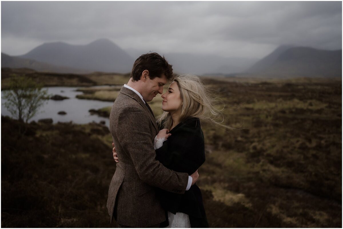 Newlyweds in a close embrace on Rannoch Moor - the bride, wrapped in a dark shawl, laughs up at the groom as he holds her close