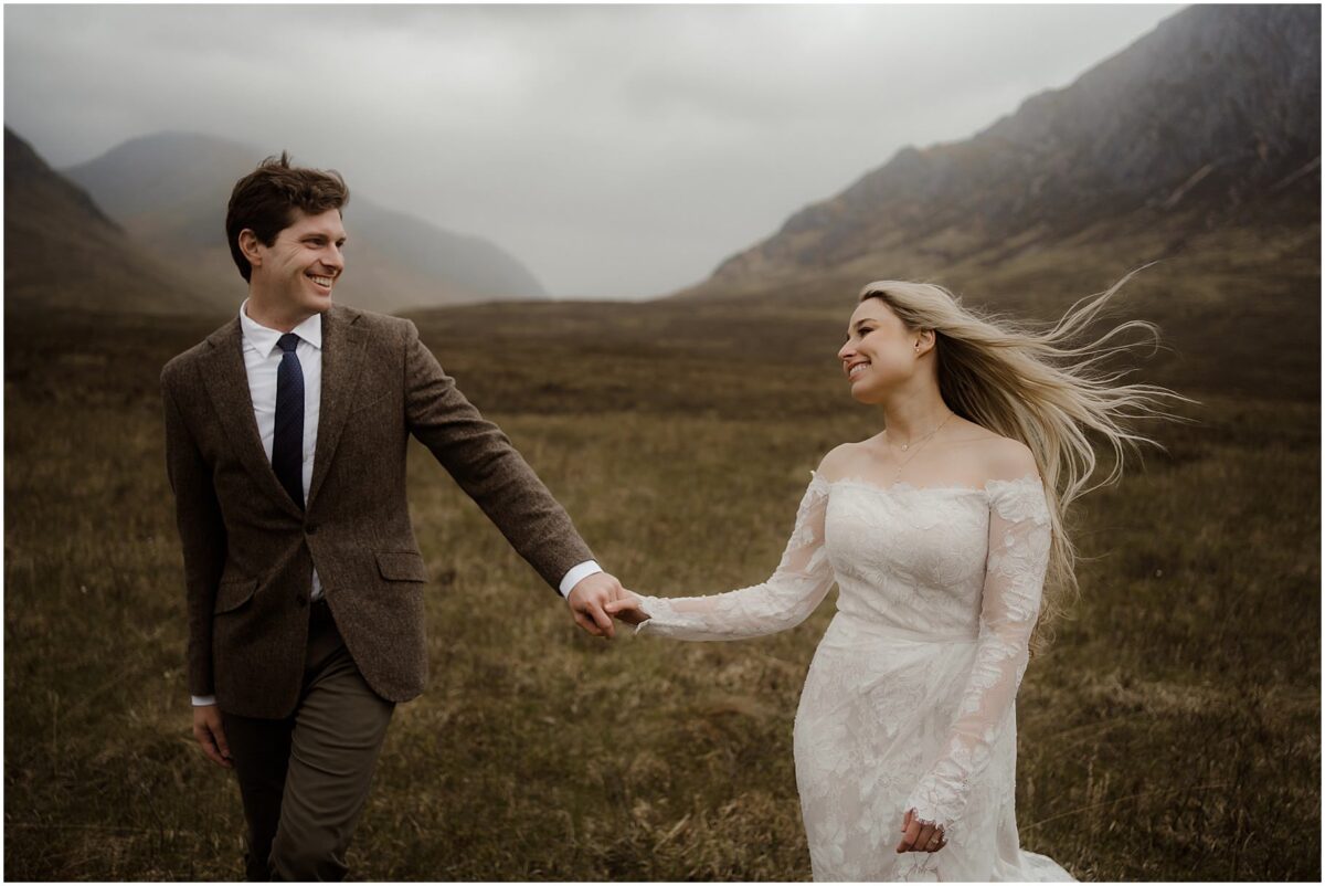 Couple holding hands and laughing whilst bride's hair dances in the wind
