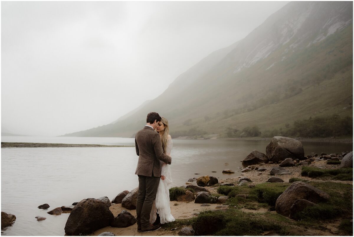 Bride and groom standing at the edge of a mist-shrouded loch
