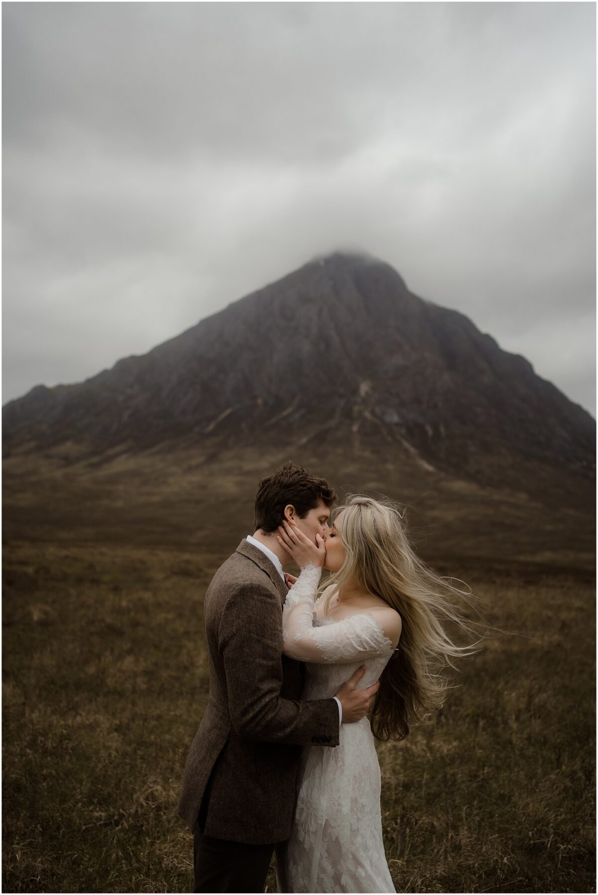 Newlyweds kissing in the open moor, Buachaille Etive Mor’s towering pyramid of rock looming dramatically behind them in the mist