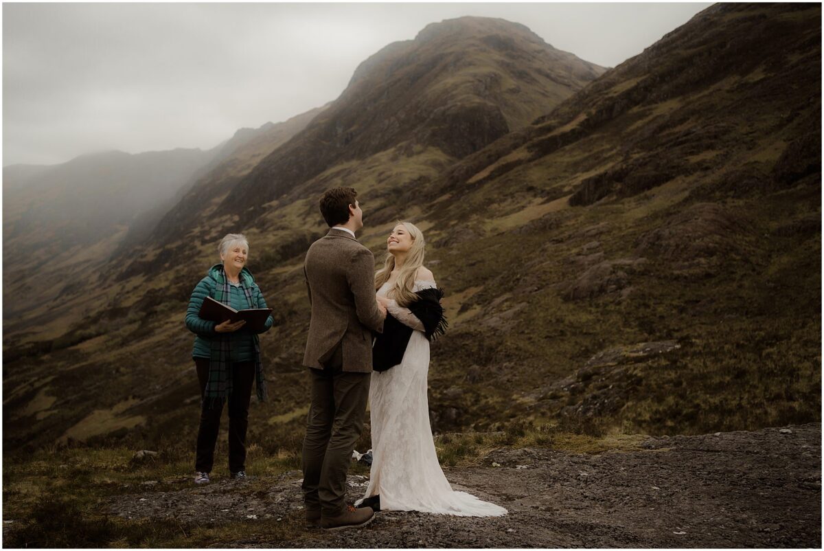 Close-up of the bride smiling through emotion as John holds her hands, officiant reading in the background