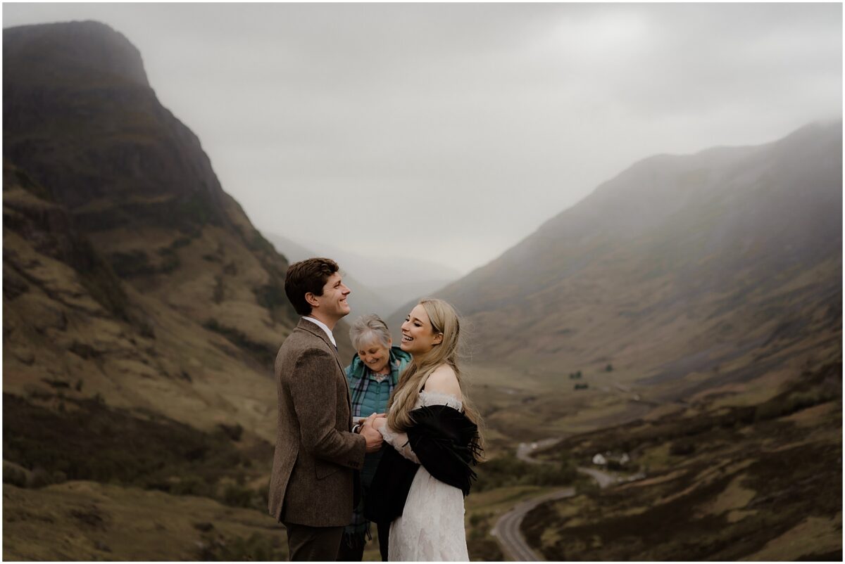 Couple laughing as mist swirls around them on a Glencoe ridgeline, valley road visible below