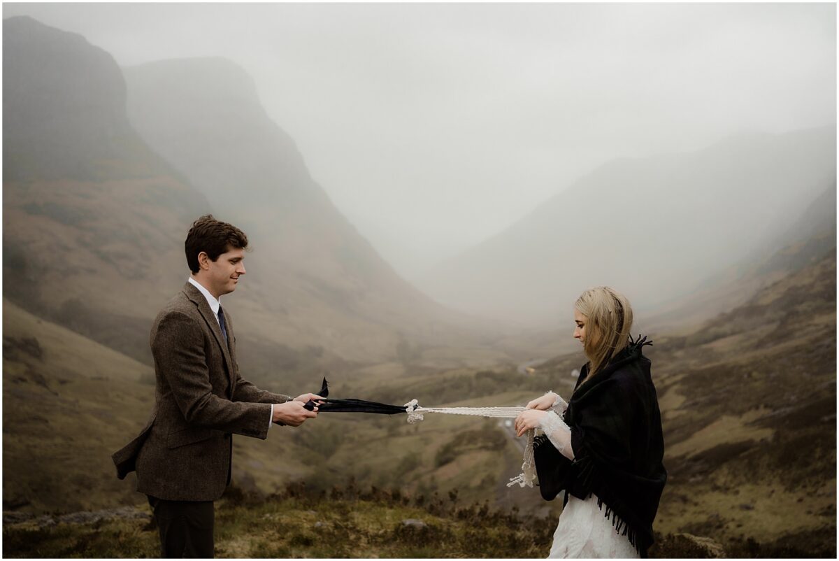 The couple pulls the braided cord taut between them in a playful tug-of-love, rugged Glen Etive peaks rising behind