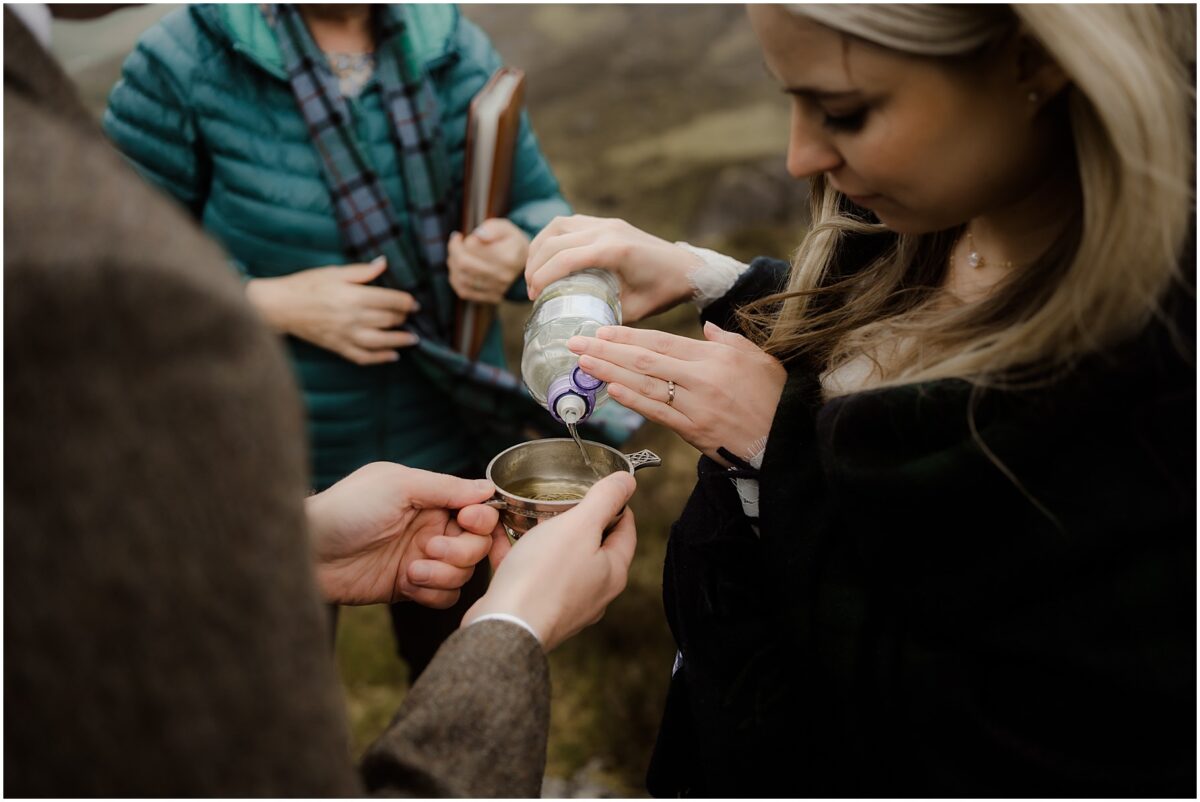 Close-up of the bride pouring water into a quaich cup, officiant holding her book in the blurred background