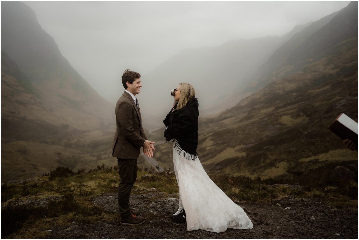 Bride takes a sip from the quaich while groom watches, green mountains and misty sky framing the scene