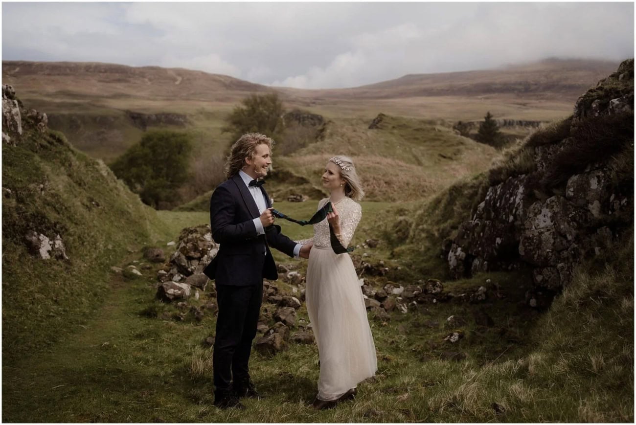 Isle of Skye elopement in Fairy Glen - Isle of Skye wedding photographer Couple laughing together holding a tartan handfasting cord in the valley at Fairy Glen, Isle of Skye