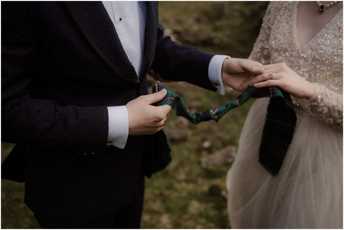 Isle of Skye elopement in Fairy Glen - Isle of Skye wedding photographer Close-up of a couple's hands holding a green tartan handfasting cord during their Scottish elopement ceremony
