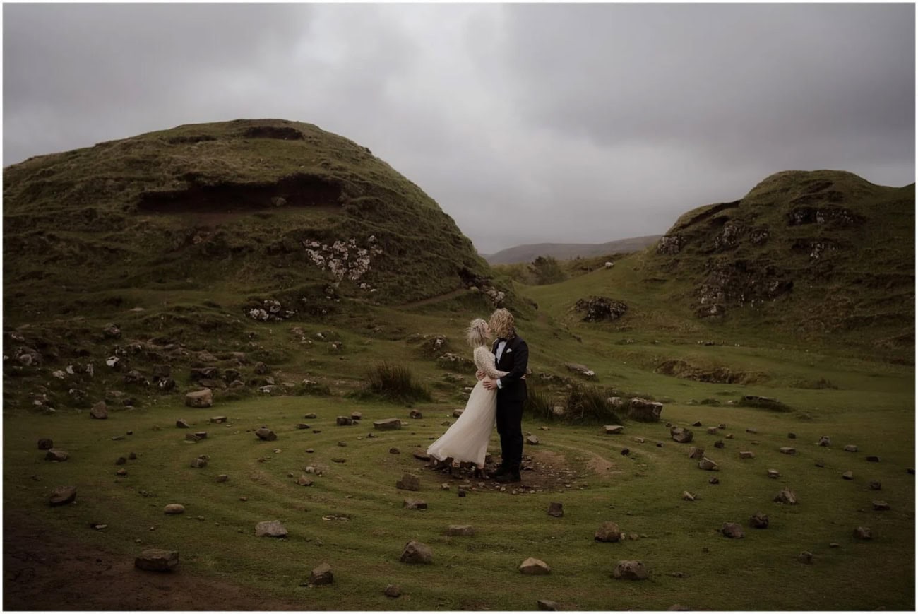 Isle of Skye elopement in Fairy Glen - Isle of Skye wedding photographer Castle Ewen rock formation at Fairy Glen, Isle of Skye, with a flock of sheep grazing below, alongside a couple walking hand in hand on the mossy hillside