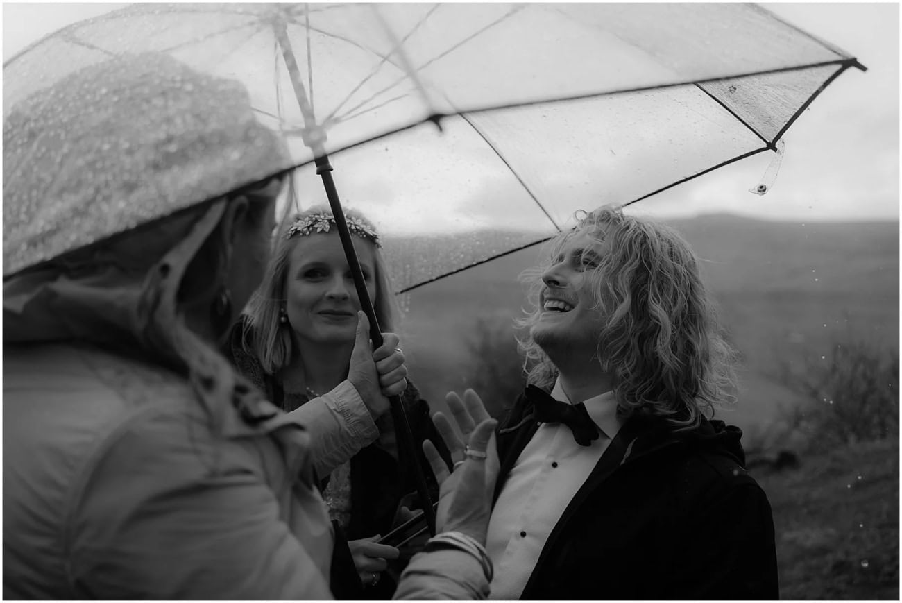 Isle of Skye elopement in Fairy Glen - Isle of Skye wedding photographer Bride and groom laughing with their celebrant under a clear umbrella during a rainy elopement ceremony at Fairy Glen, Isle of Skye, black and white