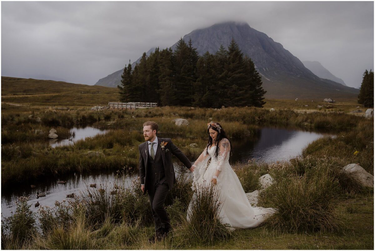 Glencoe wedding photos - Glencoe wedding photographer Bride and groom walking by the pond with Buachaille Etive Mòr towering behind them