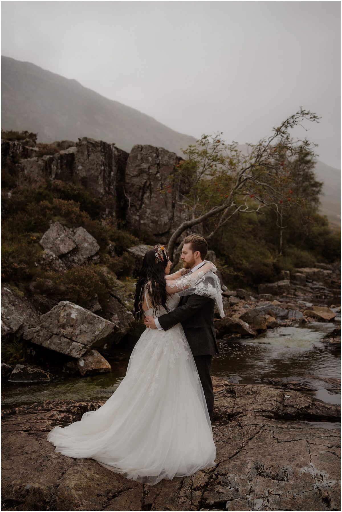 Glencoe wedding photos - Glencoe wedding photographer Couple sharing an embrace whilst standing on a rocky platform by the river in Glencoe