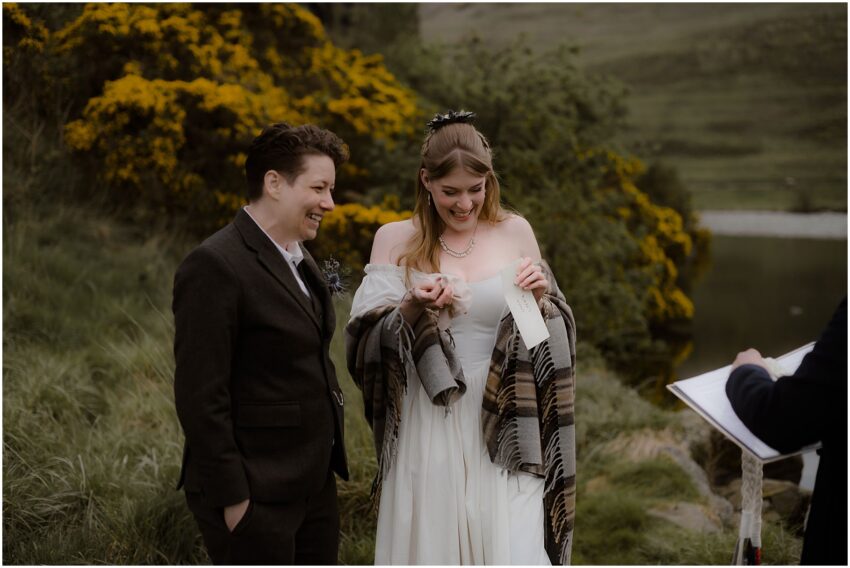 Two brides exchanging vows and laughing at their outdoor wedding in Holyrood Park in Scotland