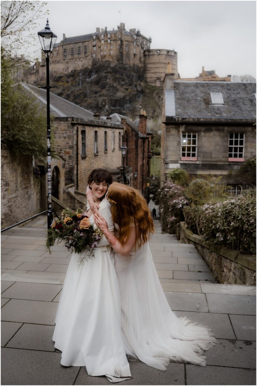 Brides hugging and laughing at the Vennel Steps with Edinburgh Castle in the background