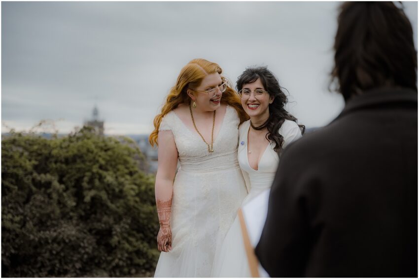 Two brides hugging and smiling during their elopement ceremony on Calton Hill in Edinburgh