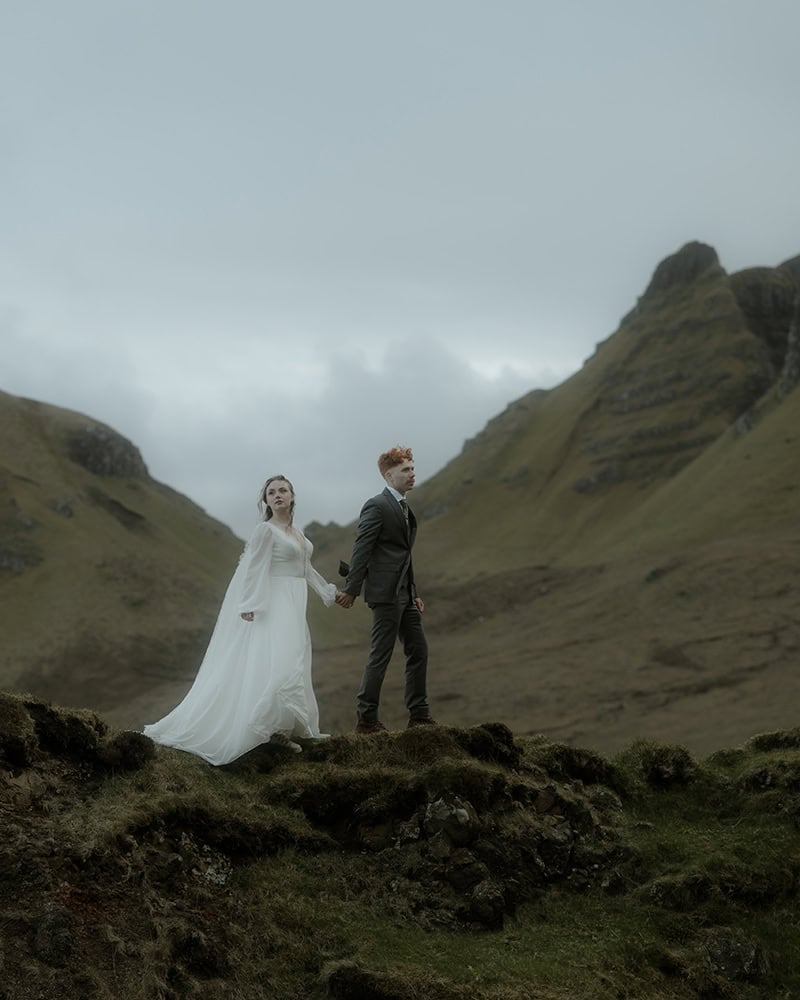 Isle of Skye Elopement Guide 2026/27 – plan your Scottish adventure wedding 29 Couple standing hand in hand on a mossy ridge at the Quiraing, Isle of Skye, looking out across the dramatic valley with mist-covered peaks rising behind them on an overcast day
