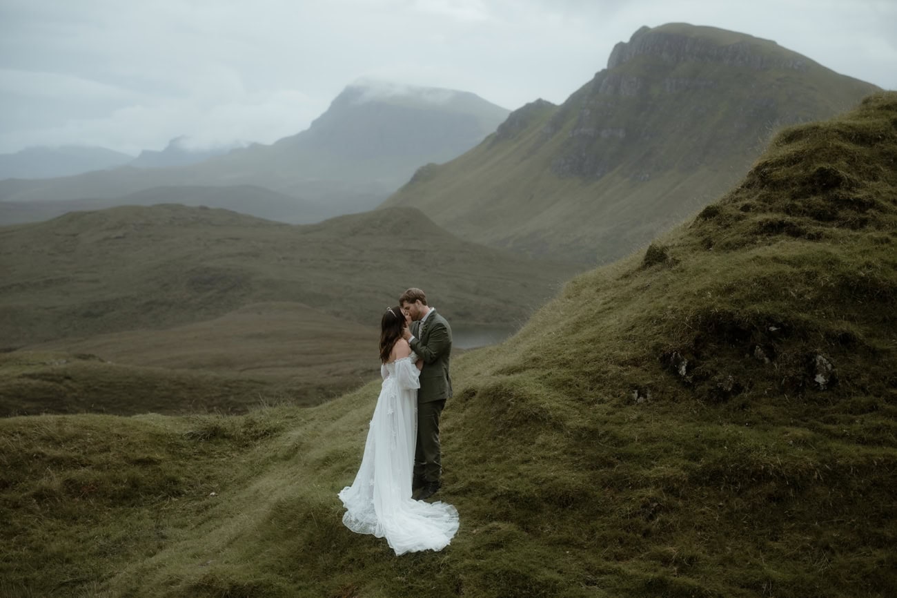 Isle of Skye Elopement Guide 2026/27 – plan your Scottish adventure wedding 4 Couple sharing their first kiss as a married couple on the mossy ridgeline at the Quiraing, Isle of Skye, with dramatic mist-covered peaks and a loch stretching into the valley behind them