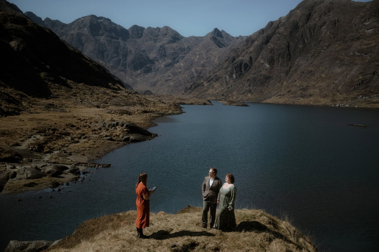 Couple exchanging vows on a rocky outcrop above Loch Coruisk during their elopement, with the full length of the loch and the towering Black Cuillin range behind them