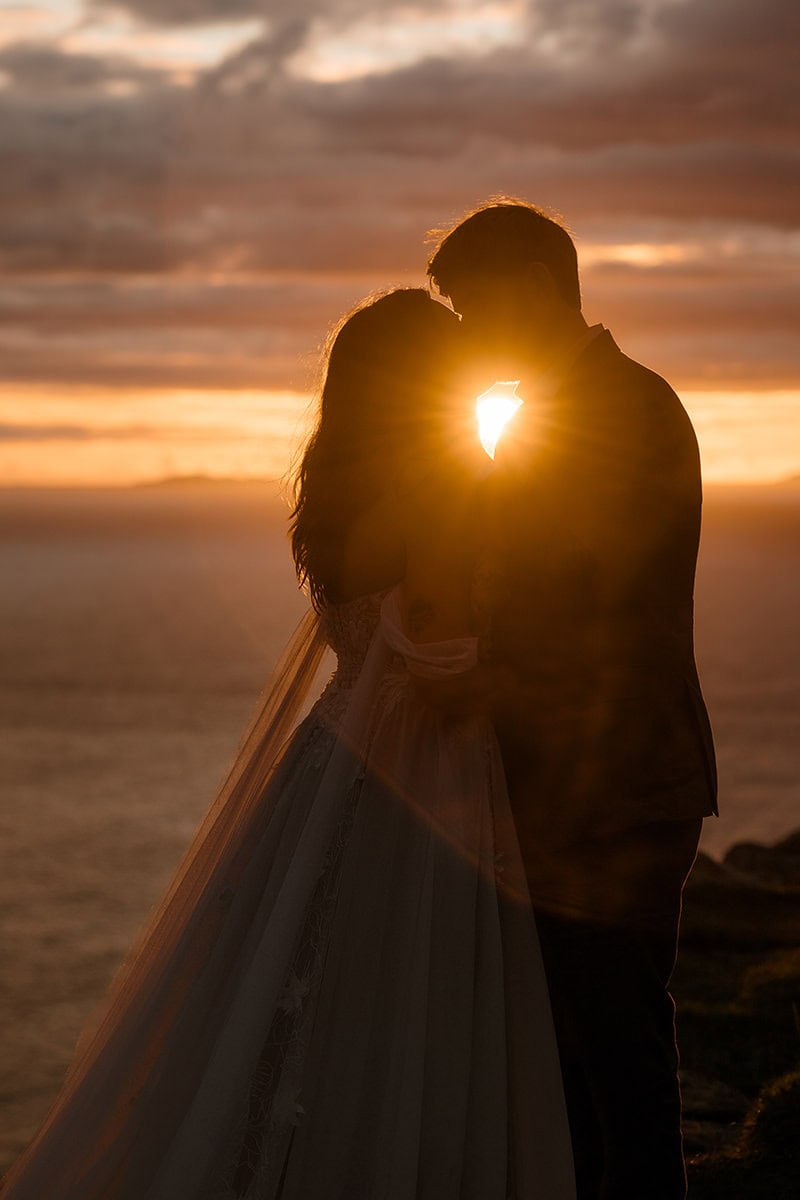 Isle of Skye Elopement Guide 2026/27 – plan your Scottish adventure wedding 15 Close silhouette of a couple leaning their foreheads together at Neist Point, Isle of Skye, the setting sun burning between them against a deep amber and rose sky