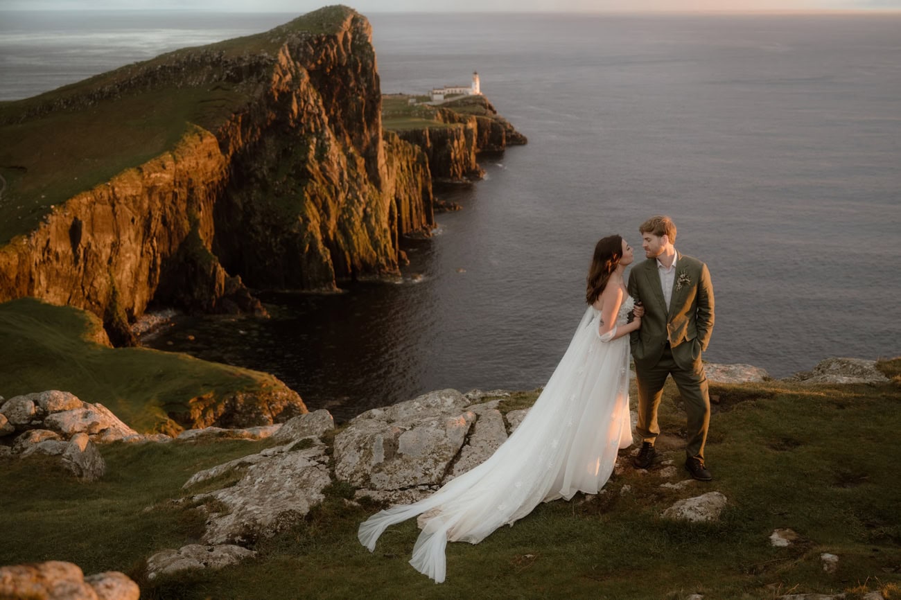 Isle of Skye Elopement Guide 2026/27 – plan your Scottish adventure wedding 13 Couple standing on the clifftop at Neist Point, Isle of Skye, at golden hour, with the lighthouse and dramatic sea cliffs stretching behind them and the Atlantic Ocean glowing in the evening light
