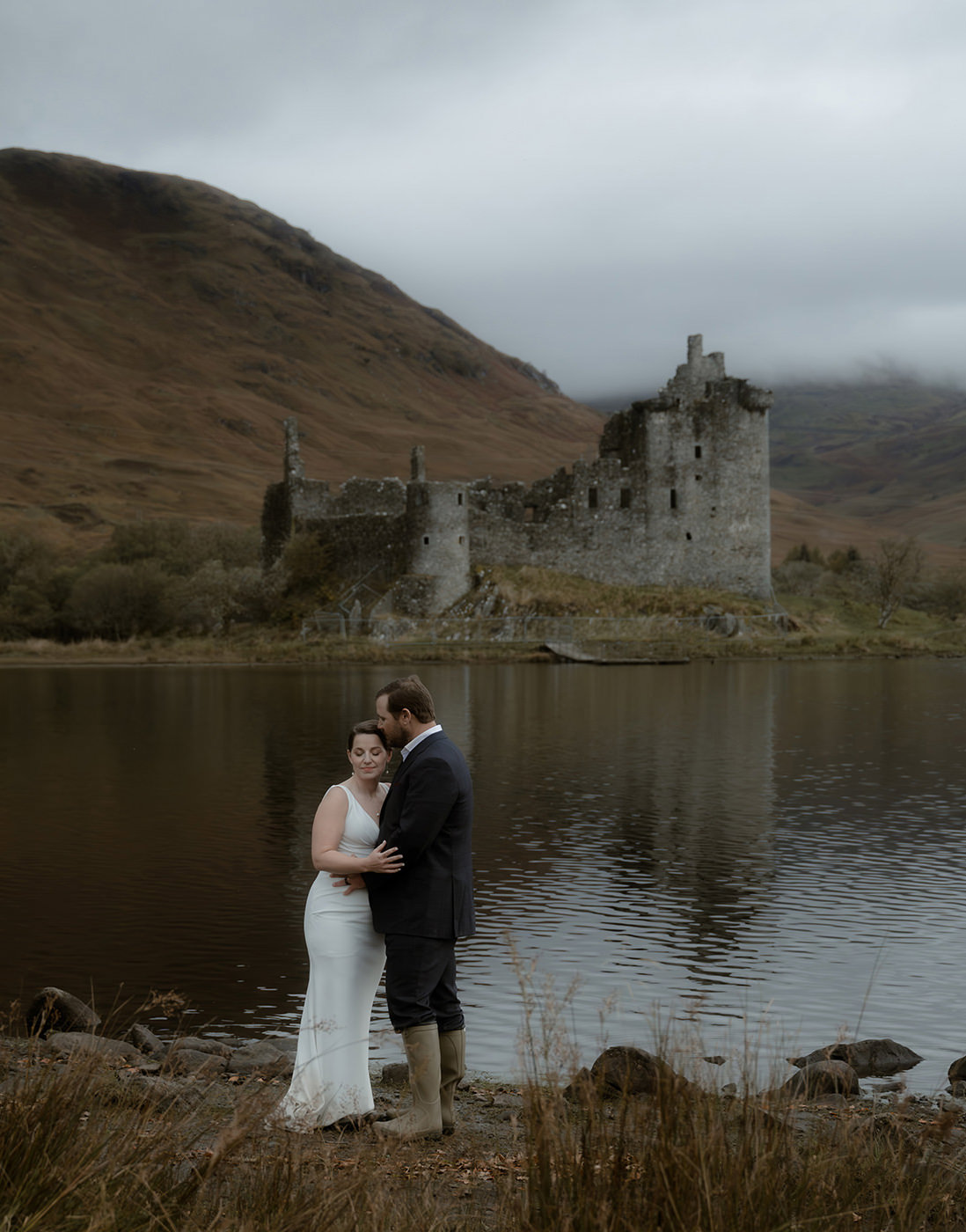 Bride and groom embracing by the lake with Kilchurn Castle ruins in the background