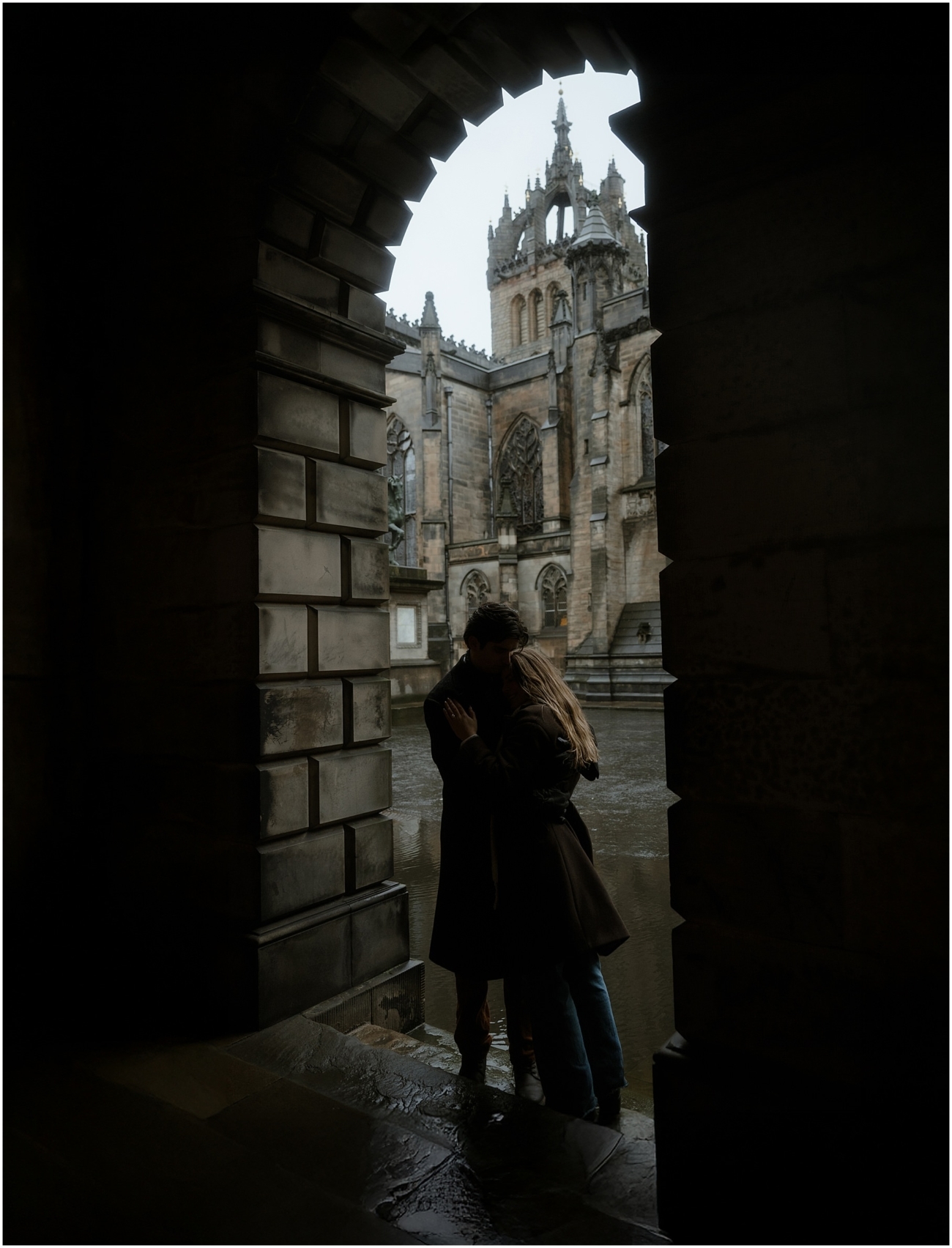 The couple stands hand in hand in front of an intricately carved historic doorway, framed by gothic stone arches with Edinburgh St Giles Cathedral in the background