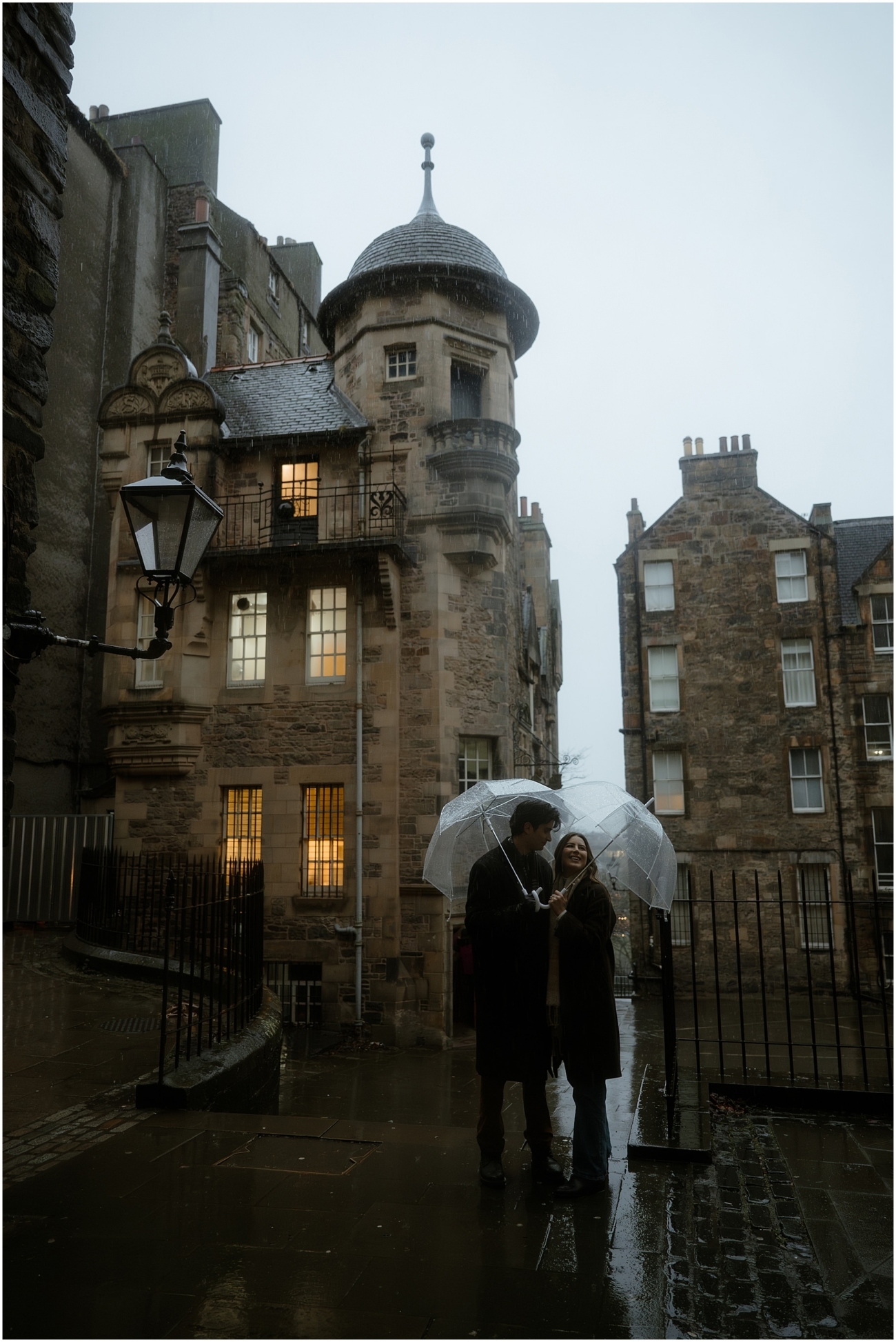 A charming scene of the couple holding hands under a transparent umbrella in front of Edinburgh Writer's Museum