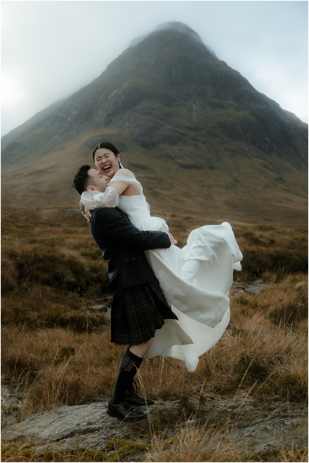 The groom lifts the bride in his arms as she laughs joyfully, her white dress flowing mid-air