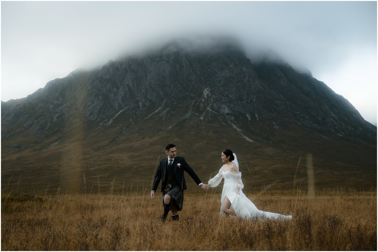 The couple holds hands as they walk through the highland terrain