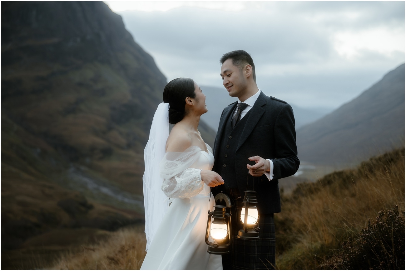 A bride and groom holding glowing lanterns, gazing at each other 