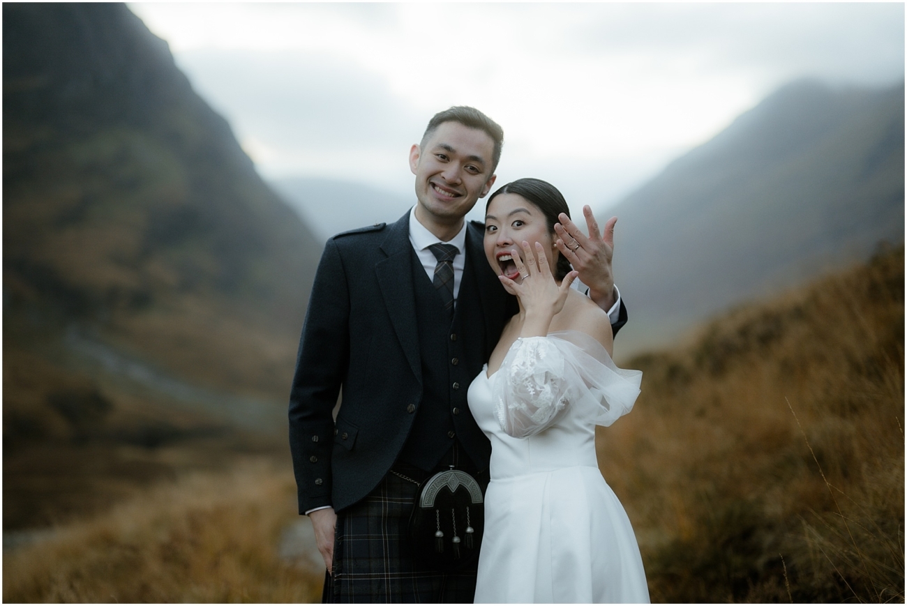 The couple playfully showing off their wedding rings, grinning